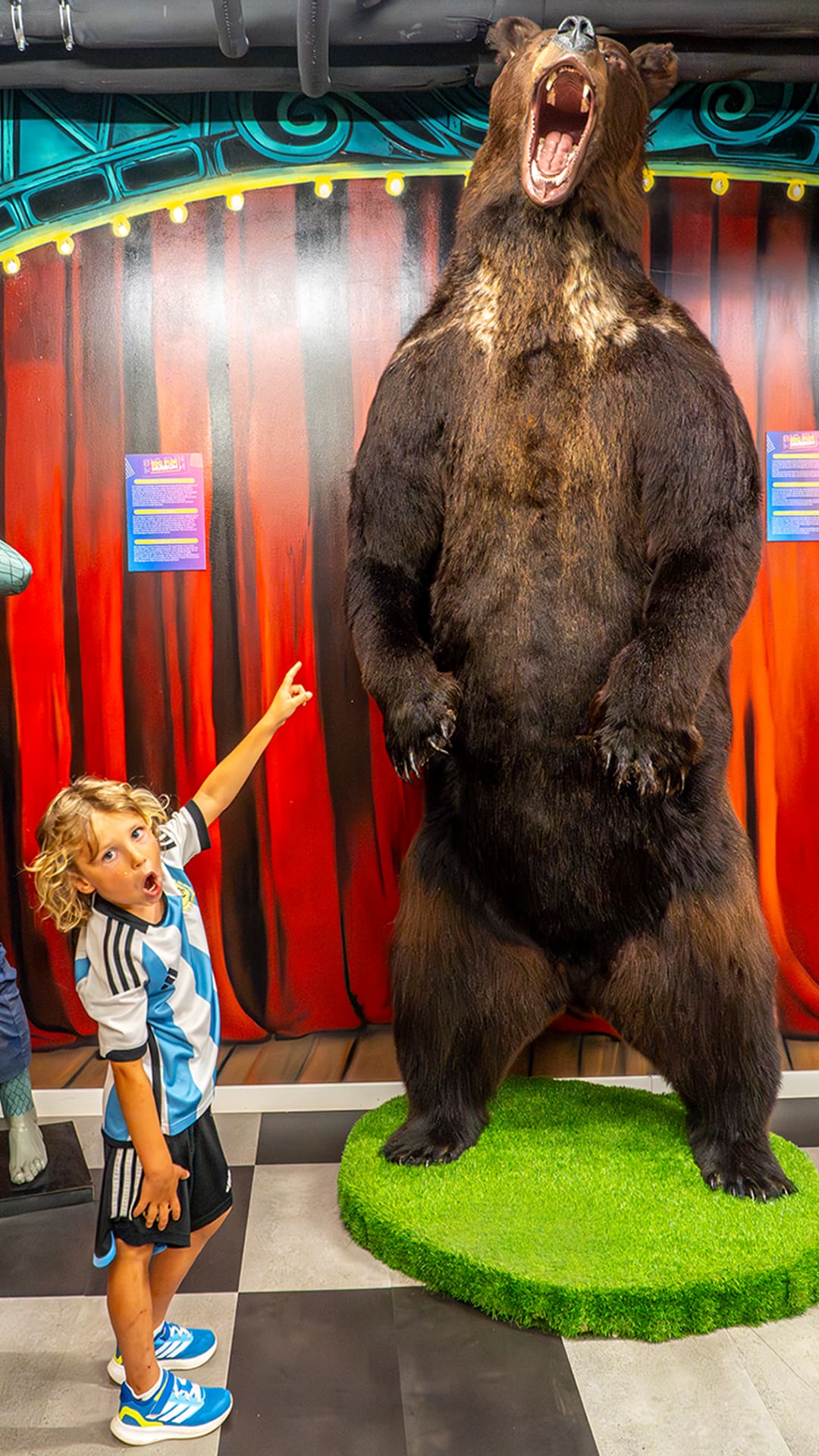 A boy pointing up in awe at a life-size grizzly bear reared on its hind legs and roaring at Guinness Records Museum Barcelona